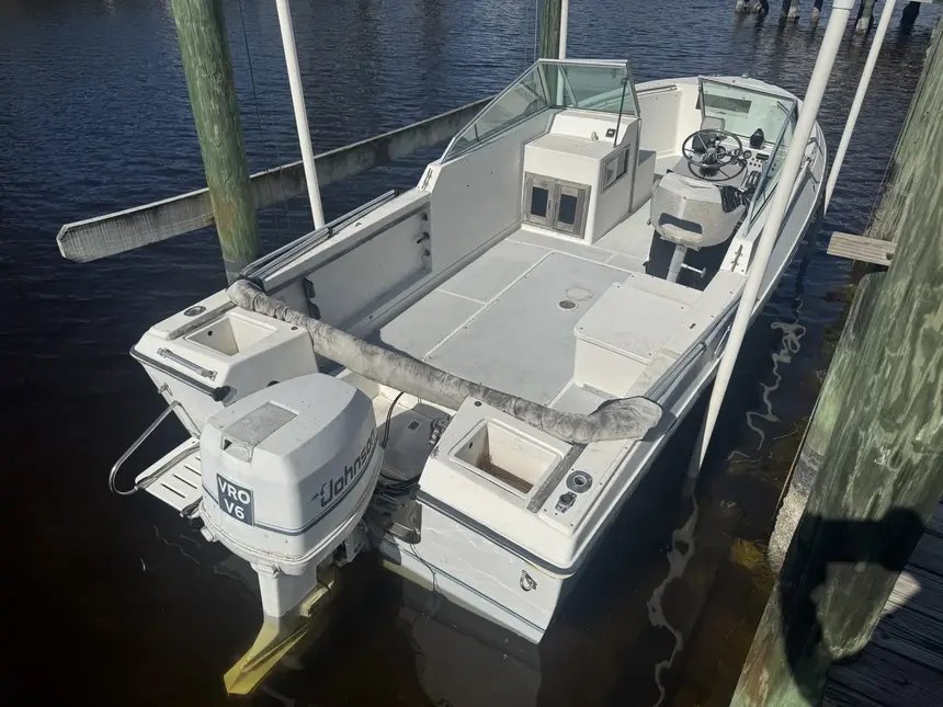  White center console boat with a Johnson VRO V6 outboard motor, docked securely at a wooden pier.